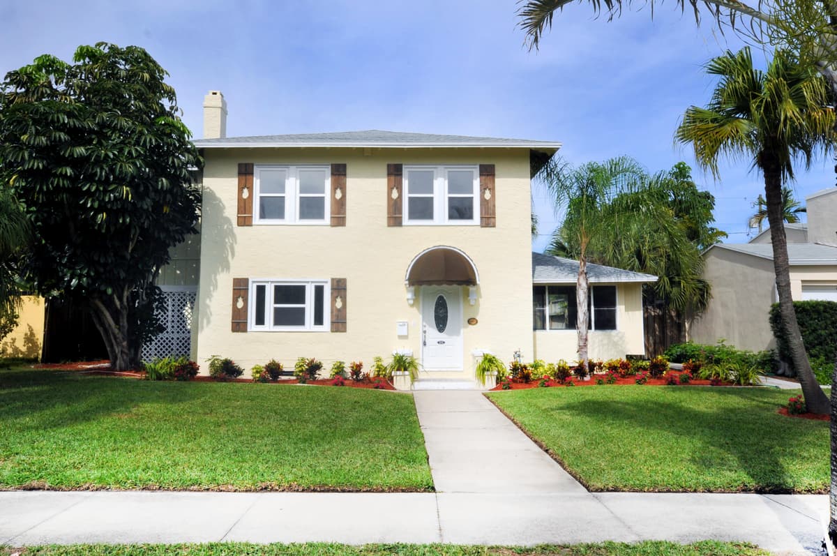Pale yellow two-story home with walnut pineapple-cutout shutters framing every window
