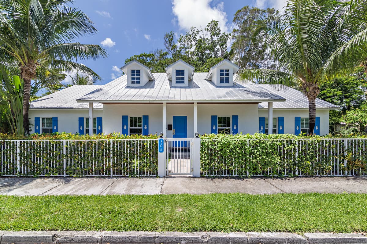 White cottage with bright blue pineapple-cutout shutters behind a vine-covered picket fence