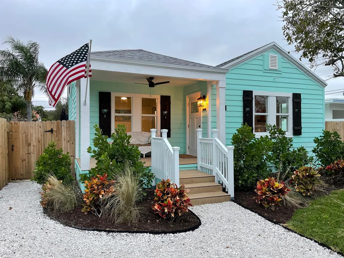Turquoise cottage with black shutters, lit porch at dusk